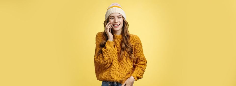 Carefree sociable good-looking outgoing woman calling friend talking happily smartphone have pleasant funny conversation smiling giggling look away hold hand pocket, standing yellow background.