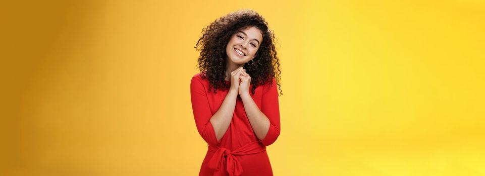So sweet love you. Portrait of tender and silly cute curly-haired young woman in red dress tilting head holding hands together near face and smiling touched during heartwarming moment of confession.