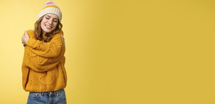 Tenderness, happiness wellbeing concept. Charming feminine cute stylish girl liking new warm sweater hugging embracing herself close eyes dreamy smiling feeling romantic coziness yellow background.