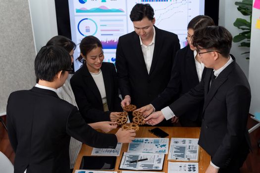 Businesspeople wearing suit for harmony synergy in office workplace concept hand holding gears into collective form with data analyzed by Bi in dashboard report papers on table.