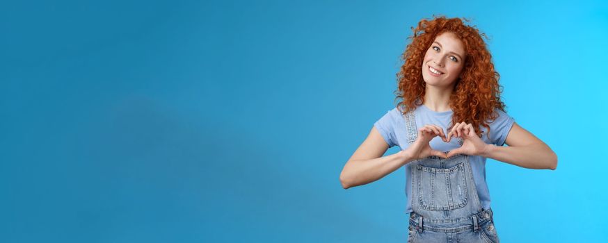 Caring tender lovely redhead girlfriend express sympathy tenderness gentle sympathy tilt head smiling broadly show heart love gesture chest cherish passionate romantic feelings, blue background.