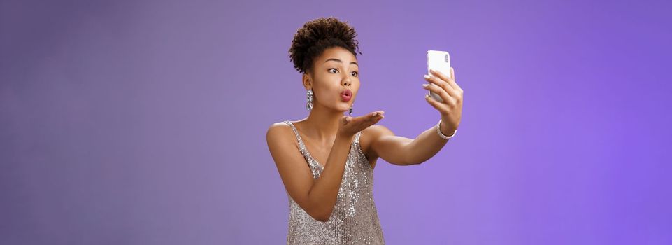 Charming elegant young female student partying enjoying prom recording video smartphone look phone display send air kiss blowing mwah taking selfie hold gadget, standing blue background.