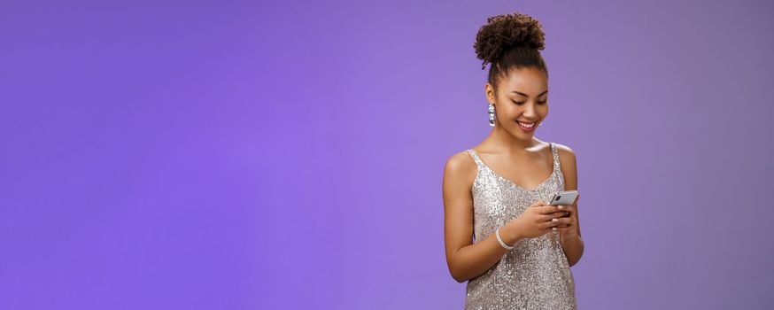 Charming elegant african-american woman. in stylish glittering prom dress writing message calling friend hold smartphone look amused happy smile phone display using gadget app scroll party photos.