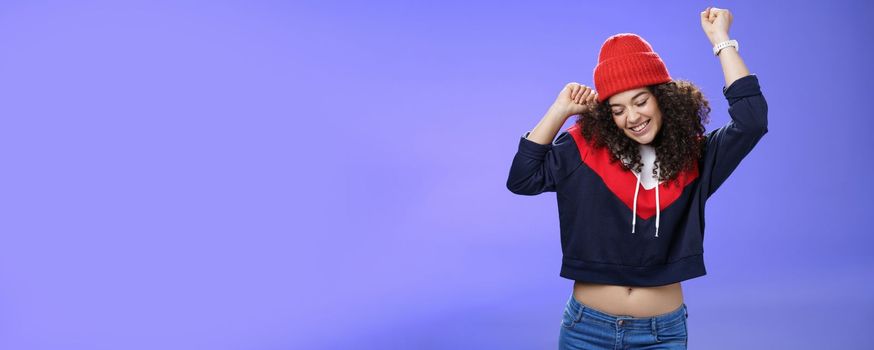 Girl celebrating favorite season in year. Portrait of carefree and joyful dancing woman with curly hair in cute red hat lifting hands in dance movements smiling enjoying music and holidays.