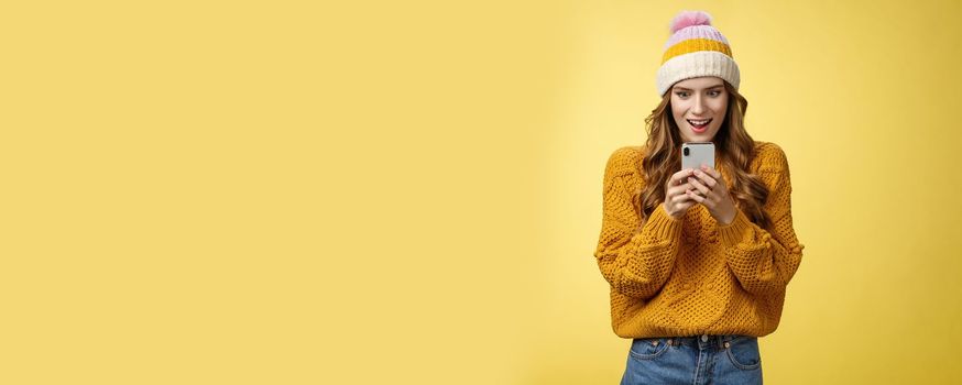 Amazed attractive stylish woman receive message smartphone awesome promotion ready shopping online smiling thrilled excited look mobile phone display, posing yellow background. Technology concept