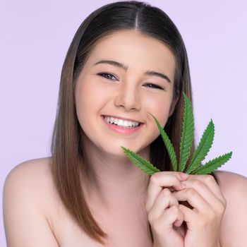 Closeup portrait of charming girl with fresh skin holding green leaf for beauty skin care made from cannabis leaf. Cosmetology and cannabis concept with isolated background.