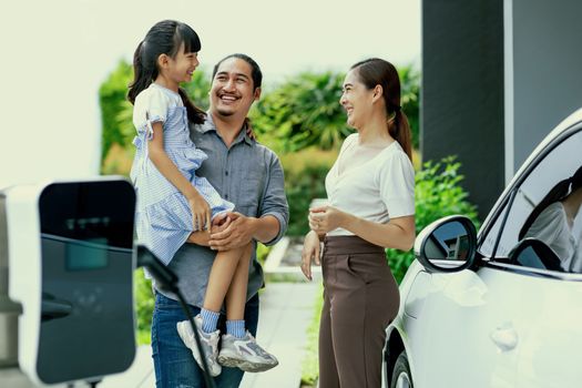 Progressive young parent teach daughter how to recharge or refuel EV car at home charging station. Green and clean energy from electric vehicle for healthy environment. Eco power from renewable source