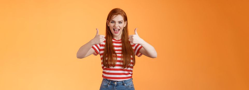 Sassy rebellious wild redhead cool girl having fun adore awesome party, show satisfactory gesture, thumb-up smiling say yeah joyfully, enjoy cool event, having fun, like idea, orange background.