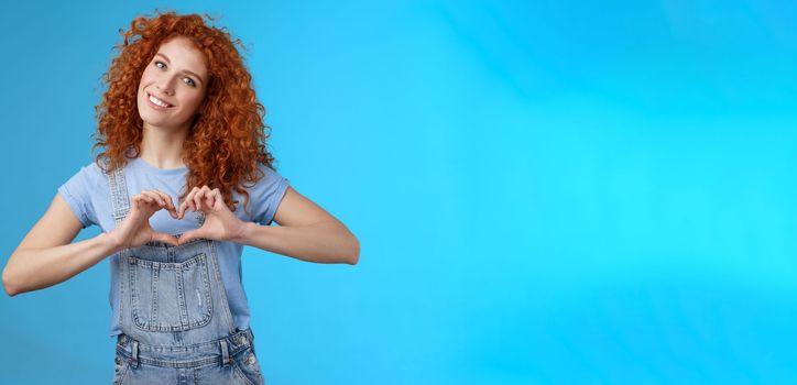 Caring tender lovely redhead girlfriend express sympathy tenderness gentle sympathy tilt head smiling broadly show heart love gesture chest cherish passionate romantic feelings, blue background.