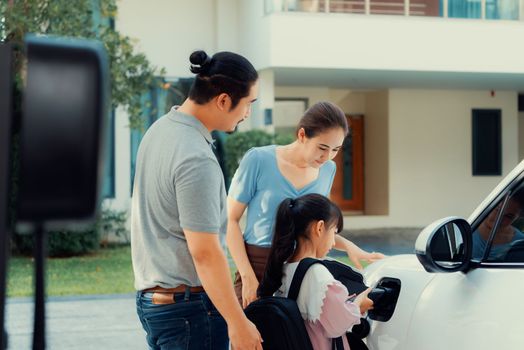 Progressive young parents and daughter with electric vehicle and home charging station. Green and clean energy from electric vehicles for healthy environment. Eco power from renewable source at home.
