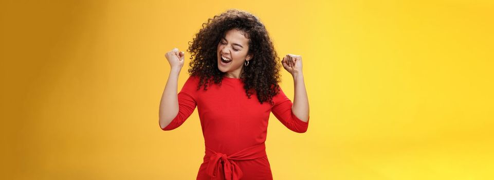 Lifestyle. Girl enjoying cool music feeling awesome as relaxing at party dancing and feeling awesome raising clenched fists saying yeah turning head joyfully with closed eyes having fun over yellow background.