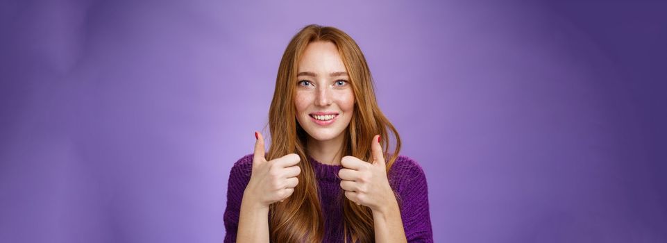 Impressed girl admiring great music taste of friend showing thumbs up and smiling excited and astonished expressing like and positive feedback, approving and supporting plan over purple background.