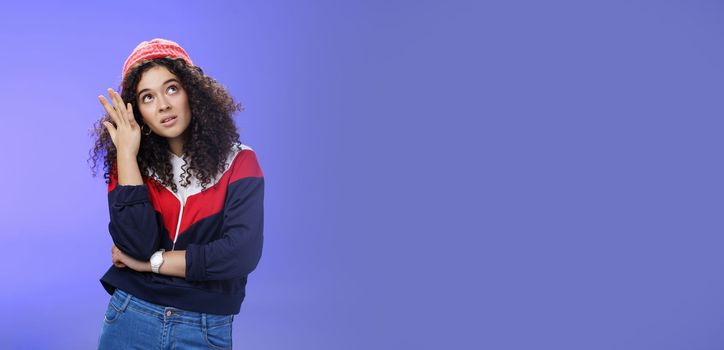 Waist-up shot of bored and annoyed assertive arrogant cool girl in streetstyle outfit rolling eyes up making facepalm and grimacing from irritation and disappointment, posing against blue background.