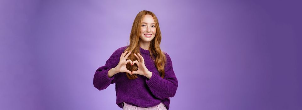 Girl loves new place to hang out, showing heart gesture and smiling satisfied and cute, expressing sympathy and admiration looking romantic and dreamy against purple background.