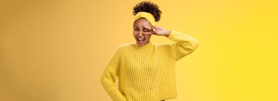 Friendly self-assured energetic african-american smiling healthy girl winking positive attitude grinning cheerful show peace victory lucky gesture hold hand waist confident, yellow background.