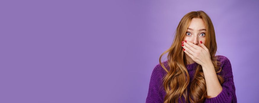 Lifestyle. Impressed speechless cute ginger girl hearing stunning gossip covering mouth form amazement and shook raising eyebrows wondered as reacting to unexpected revelation or rumor over purple background.