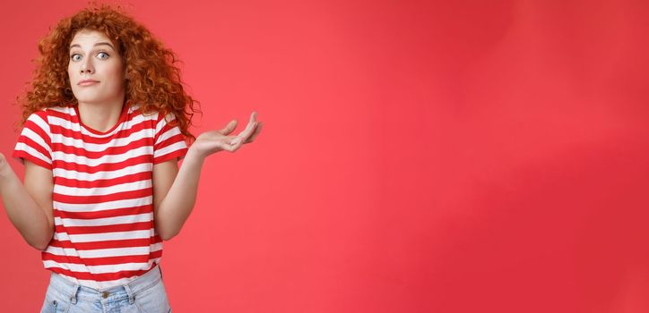 Not know ask someone else. Clueless unaware cute redhead curly-haired charming modern girl uncertain where spend summer holidays shrugging hands spread sideways smirking confused red background.