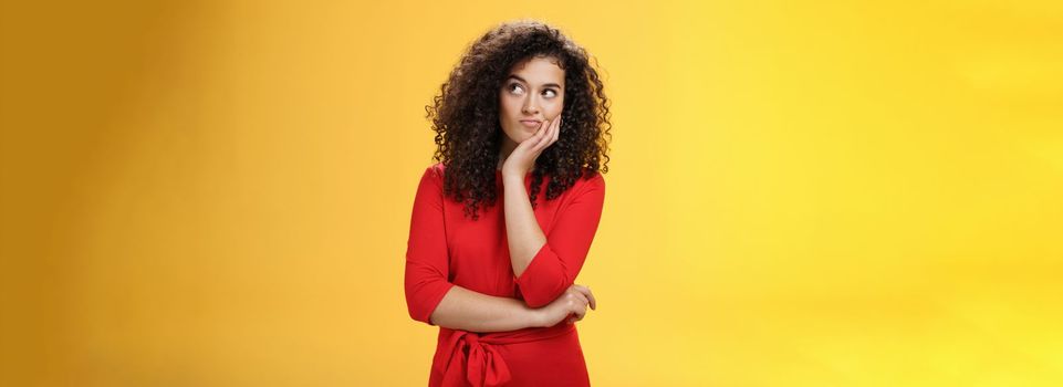 Waist-up shot of cute girlfriend scheming feeling bothered with some idea or thought smirking looking right interested and impatient as making up plan standing thoughtful over yellow background. Copy space