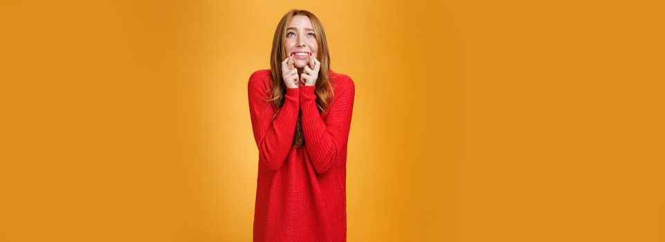 Lifestyle. Portrait of excited and worried young redhead female in 20s stooping standing in begging pose crossing finger for good luck looking at sky as praying god and asking help with wish come true.