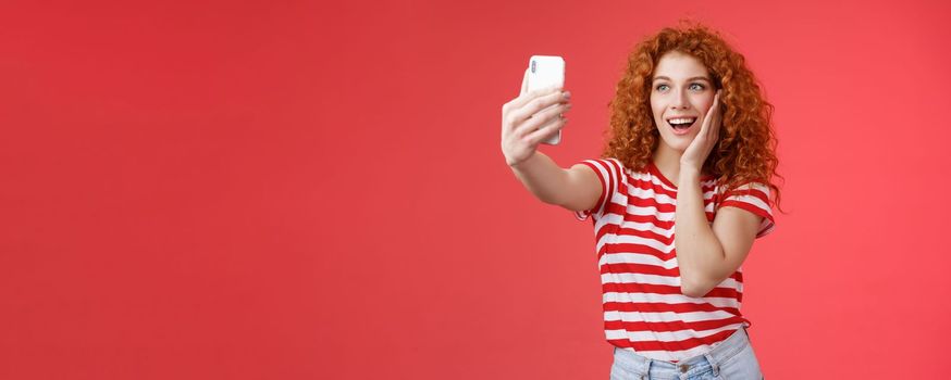 Lifestyle. Fashionable cute redhead curly female summer t-shirt record video social media from luxury tropical resolt travel holidays abroad take selfie hold smartphone pose silly photograph red background.