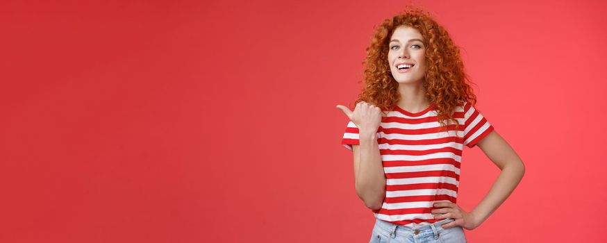 Accomplished good-looking redhead curly woman raise head proudly confident pointing thumb left smiling camera assertive sharing awesome product location recommend perfect store offer.