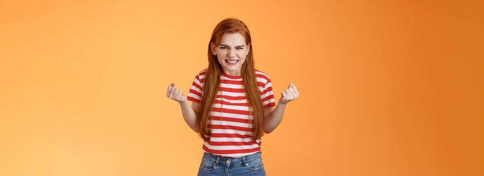 Annoyed pissed redhead female lose competition, clench fists angry grimacing evil hateful face, pressured, hate unfair results, stand orange background bothered, depressed and irritated.