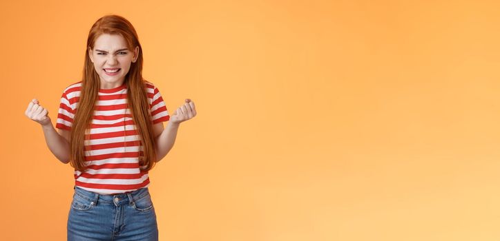 Annoyed pissed redhead female lose competition, clench fists angry grimacing evil hateful face, pressured, hate unfair results, stand orange background bothered, depressed and irritated.