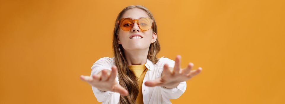 Girl reaching with desire at camera wanting grab it. Portrait of good-looking stylish caucasian young woman in trendy sunglasses biting lip from will to have something pulling hands towards. Body language concept