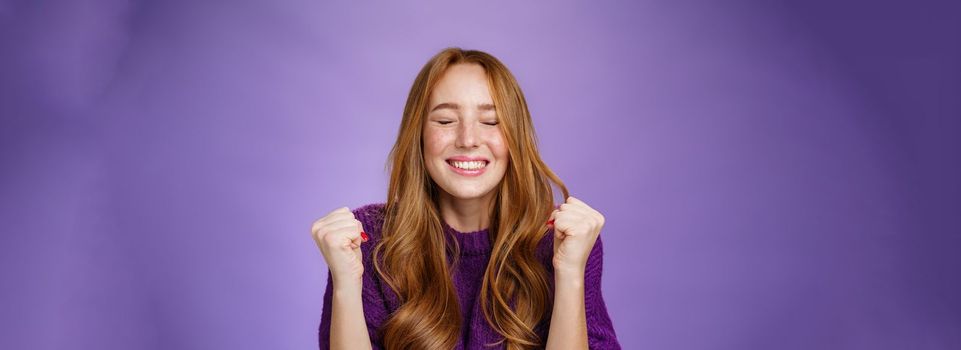 Finally I won. Portrait of relieved and happy triumphing good-looking redhead woman clenching fists in joy and happiness, celebrating victory and cheering with closed eyes and satisfied smile.