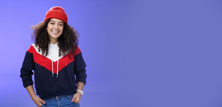 Girl invites join her team to srow snowballs. Portrait of friendly-looking carefree joyful woman with curly hair in red cute beanie and warm sweatshirt smiling joyfully getting ready for winter. Emotions, weather and fashion concept