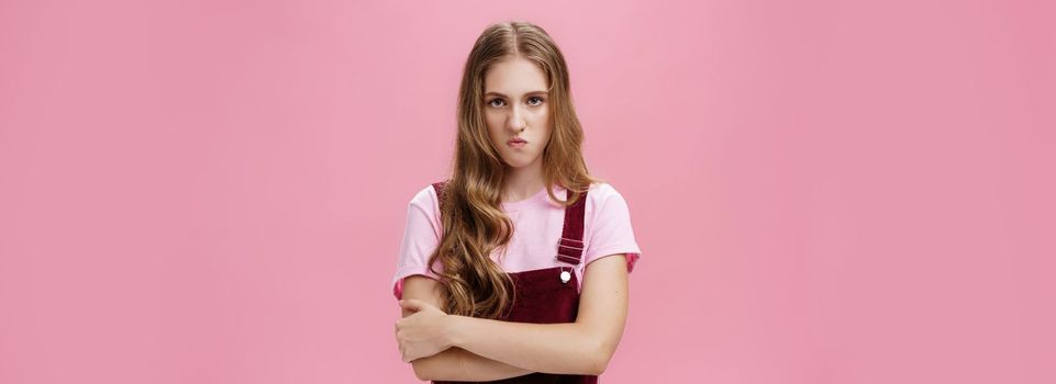 I mad on world. Unhappy hateful young arrogant girl in overalls with wavy natural hairstyle crossing arms against chest in defensive pose lifting upper lip in scorn and disdain, looking with anger. Emotions concept