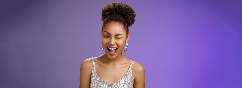 Attractive stylish wealthy african american woman in luxurious earrings silver dress winking asssuring everything ok guarantee your secret safe smiling devious have excellent plan, blue background.