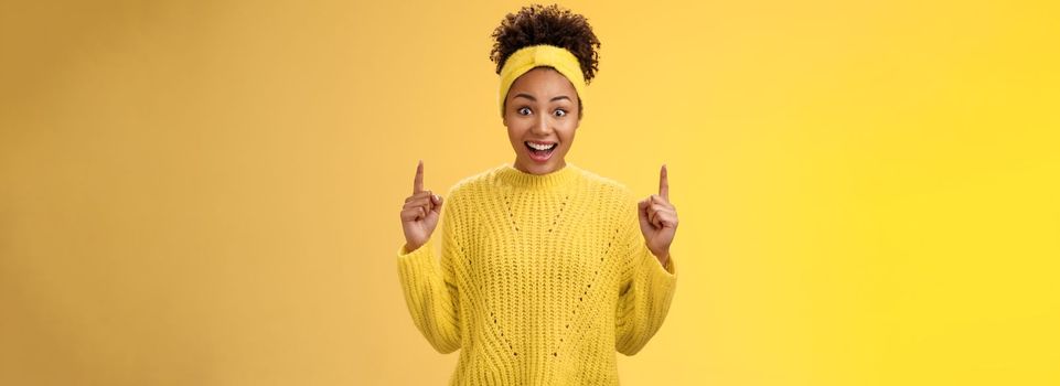 Astonished impressed african-american girl drop jaw amused widen eyes surprised pointing up index fingers reacting incredible amazing discount sale shopping center, standing yellow background.