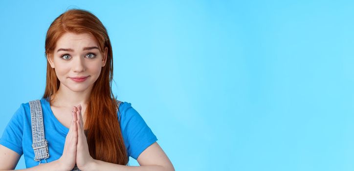 Close-up attractive tender redhead woman asking pretty please, supplicating, hold hands pray, namaste gesture, look sincere pity, smiling begging help favor, stand blue background. Copy space