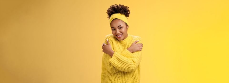 Attractive tender gentle african-american teenage girl in sweater headband hugging herself hands touch shoulders feel warm safe cozy smiling happily embracing cuddling lovely giggle. Copy space