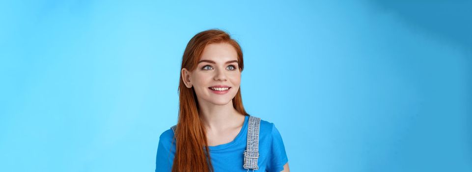 Dreamy creative cheerful redhead woman contemplate sky, smiling upbeat, rejoice good summer weather, gaze up happy, grin satisfied, observe interesting promo, stand blue background.