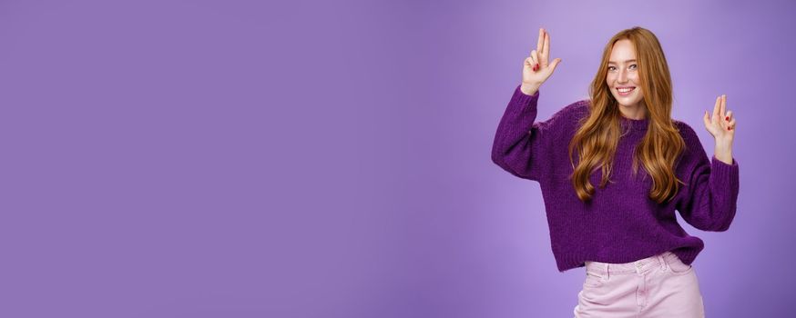 Lifestyle. Girl in happy and energized mood dancing having fun making finger pistols gesture as smiling flirty at camera feeling thrilled and joyful at awesome party posing in purple sweater over violet wall.