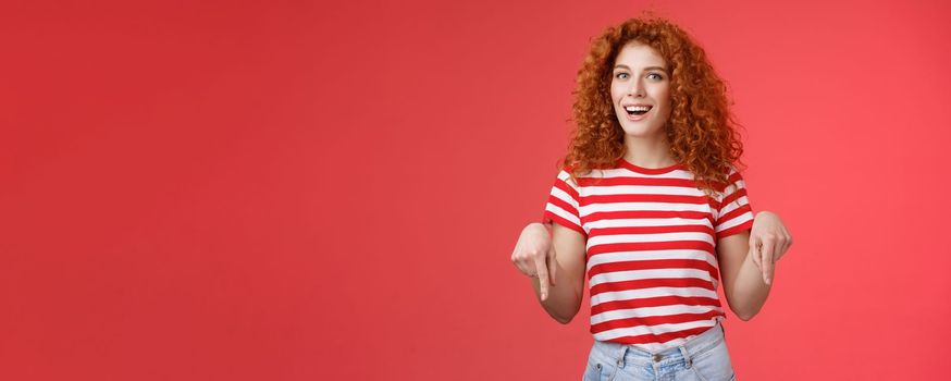 Hey check it out friend. Sassy good-looking cheeky redhead stylish girlfriend curly hairstyle wear summer t-shirt pointing down index finger smiling amused delighted present awesome recommendation.