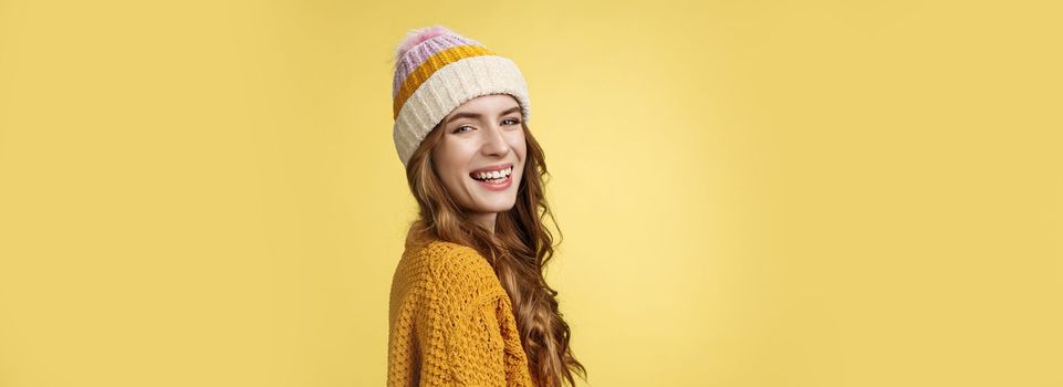 Profile shot charming carefree happy smiling girl turning camera grinning joyfully enjoying winter vacation having fun skiing, standing amused laughing wearing hat knitted sweater yellow background.