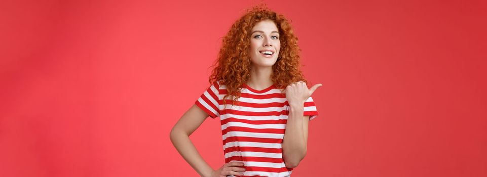 Accomplished good-looking redhead curly woman raise head proudly confident pointing thumb left smiling camera assertive sharing awesome product location recommend perfect store offer.