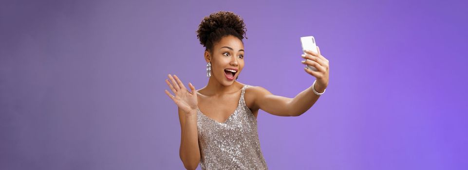 Friendly stylish confident african-american woman in silver glittering dress waving raised palm hello hi gesture record video smartphone greeting internet followers blogging during party.