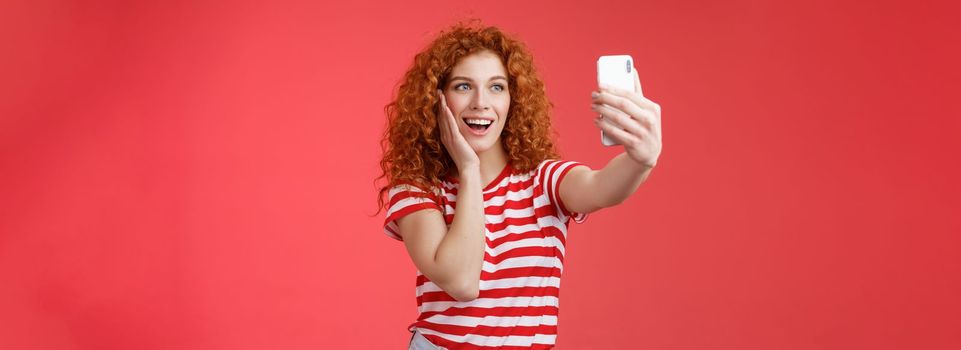 Lifestyle. Fashionable cute redhead curly female summer t-shirt record video social media from luxury tropical resolt travel holidays abroad take selfie hold smartphone pose silly photograph red background.