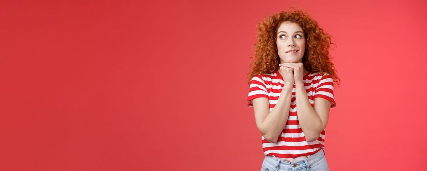 Cheerful intrigued redhead silly curly-haired woman smiling interested hold hands chin face-line imaging thinking about tasty burger look away desire have bite standing red background. Copy space