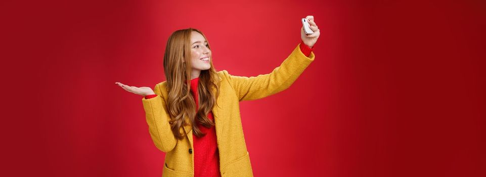 Cute redhead woman walking in park deciding take selfie near beatiful scenery or cute animal extending hand with smartphone smiling broadly at device as taking photo and pointing at something. Technology and lifestyle concept