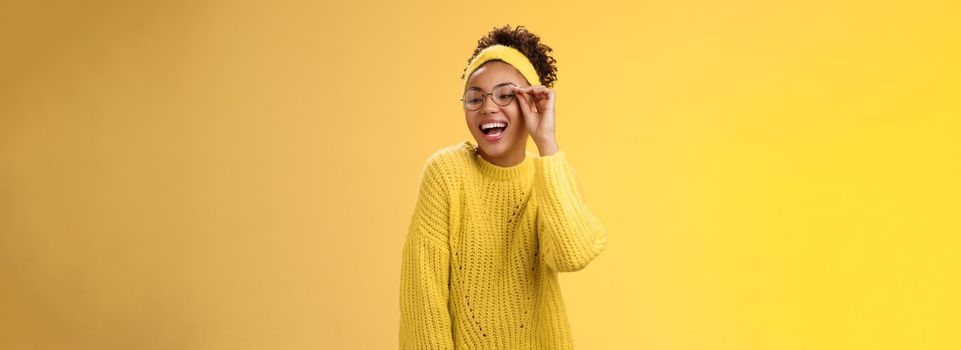Charismatic stylish confident beautiful african-american joyful teenage girl touching glasses nose laughing broadly look down right corner grinning have fun joking enjoying, yellow background.