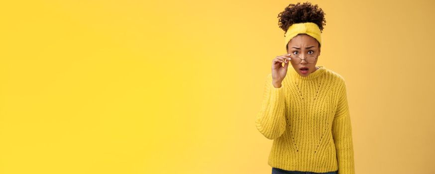 Shocked amazed african-american female student drop jaw gasping concerned confused take-off glasses bending forward reassure see truth, standing impressed speechless, yellow background.