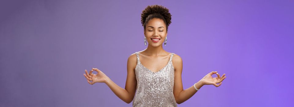 Happy relieved elegant african american woman. luxurious evening silver glittering dress smiling happily feel rejoice stress-free calm down meditating breathing excercise find nirvana yoga pose.