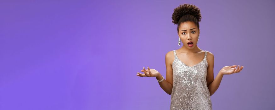 Confused worried upset african-american stylish female party host in silver shiny dress raising hands dismay look questioned sad friend leaving standing wondered frustrated, talking blue background.