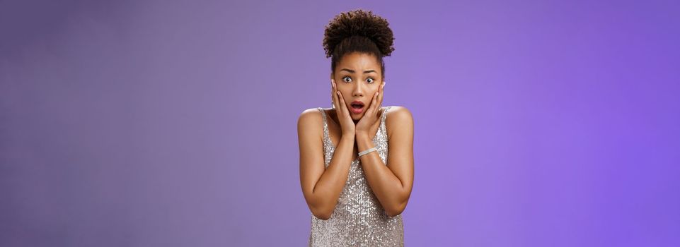 Shocked stunned speechless young african-american female friend gasping widen eyes drop jaw touch cheeks empathy look camera worry for terrible accident, standing astonished blue background.