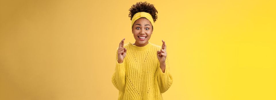 Excited optimistic hopeful young timid african-american girl. in yellow sweater smiling broadly thrilled anticipating good news bealive fortune cross fingers good luck grinning expect good news.